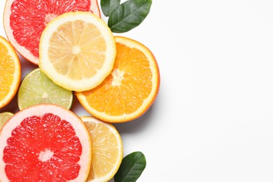 Photo of Different cut citrus fruits and leaves on white table, flat lay. Space for text