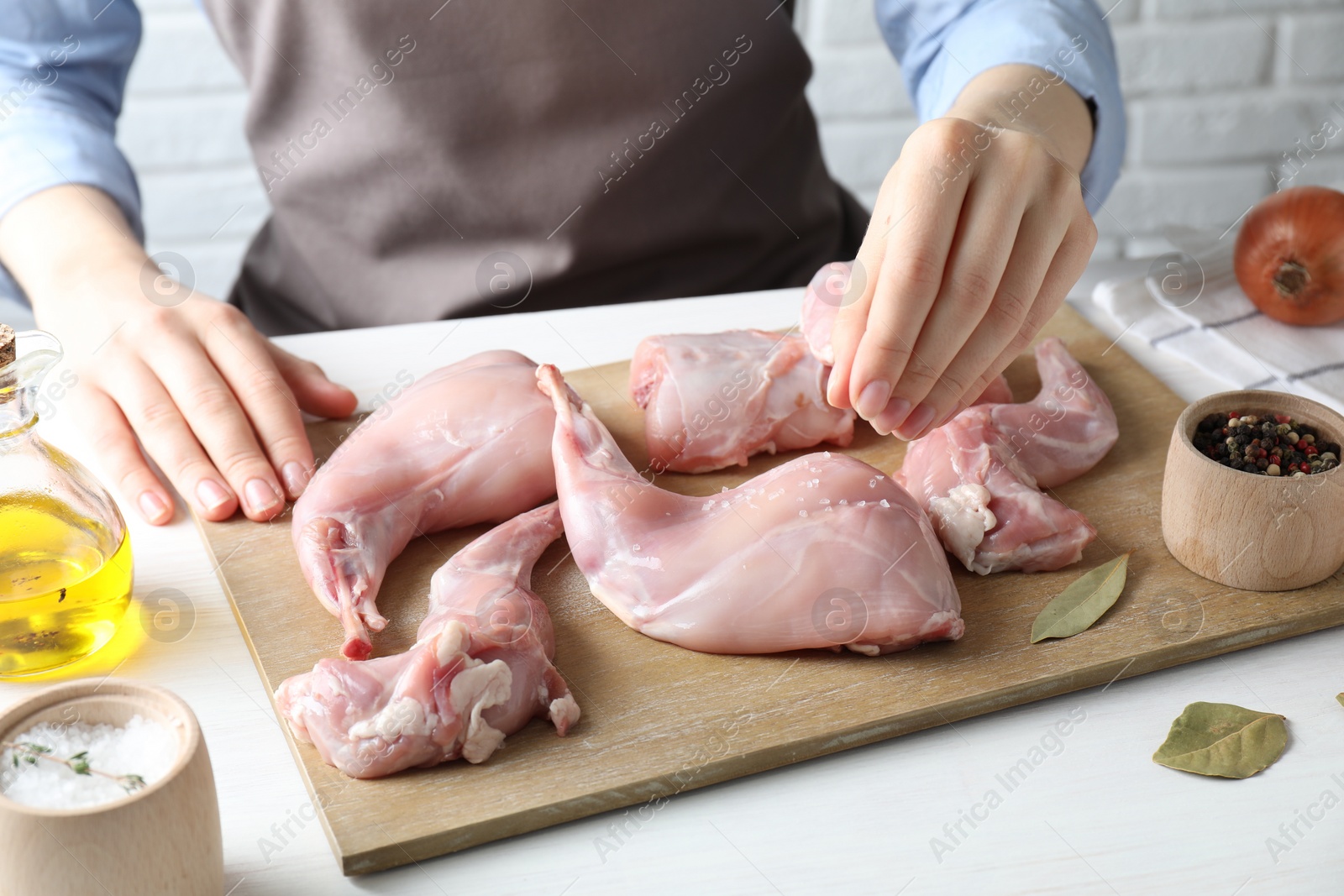 Photo of Woman putting salt onto raw rabbit meat at white wooden table, closeup
