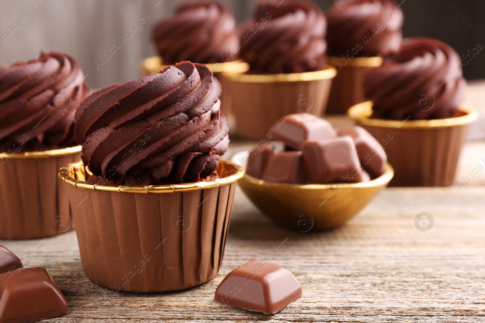 Photo of Delicious cupcakes and chocolate pieces on wooden table, closeup