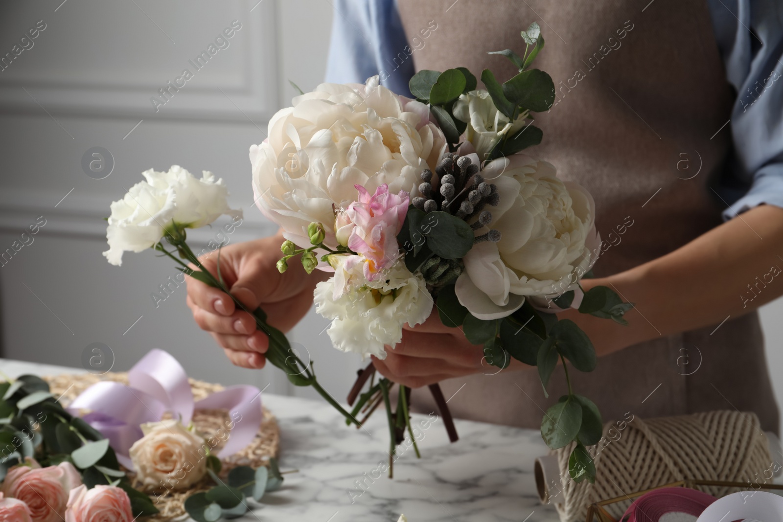 Photo of Florist creating beautiful bouquet at white marble table, closeup