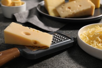 Grated, whole pieces of cheese and grater on dark textured table, closeup