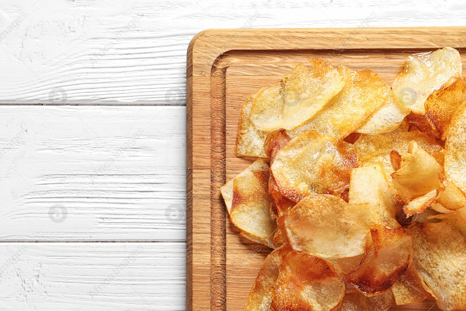 Photo of Wooden board with crispy potato chips on table, top view