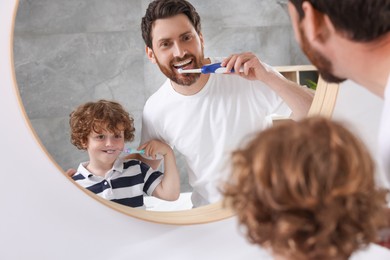 Father and his son brushing teeth together near mirror indoors