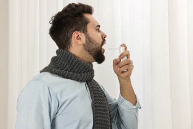 Photo of Young man with scarf using throat spray indoors