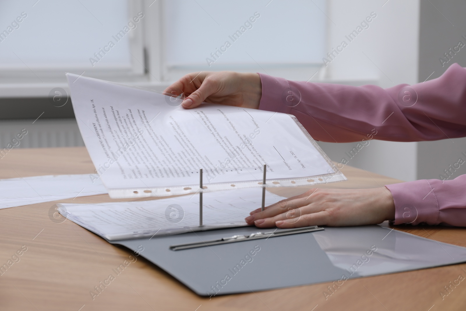 Photo of Woman putting punched pocket with document into folder at wooden table, closeup