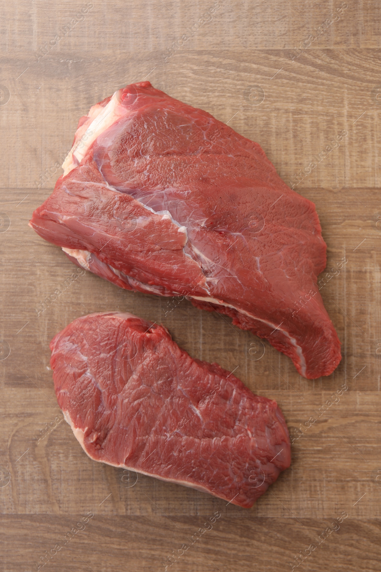 Photo of Pieces of raw beef meat on wooden table, flat lay