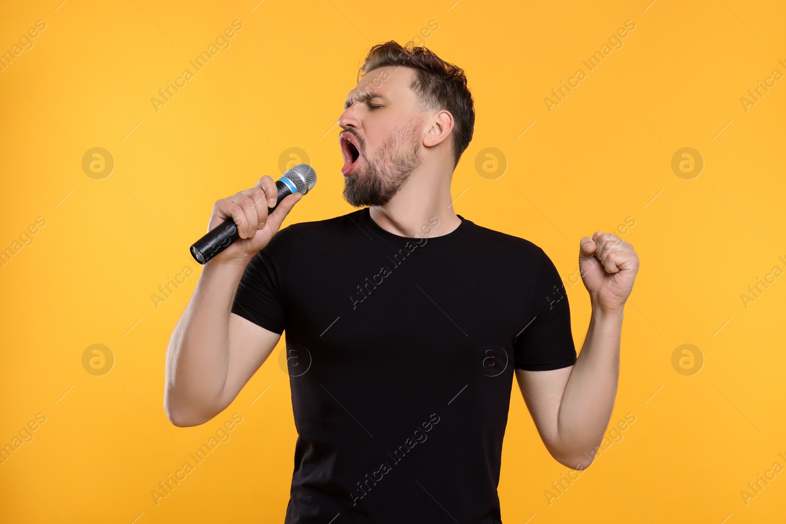 Photo of Handsome man with microphone singing on yellow background