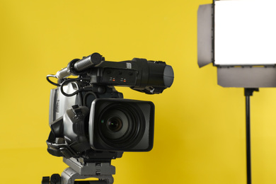 Photo of Professional video camera and lighting equipment on yellow background