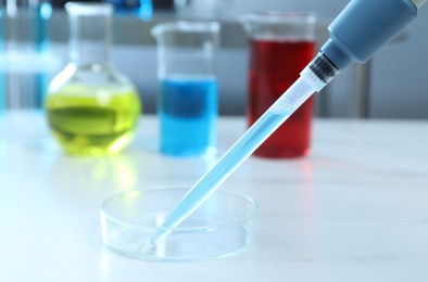 Photo of Laboratory analysis. Micropipette with liquid and petri dish on white table, closeup