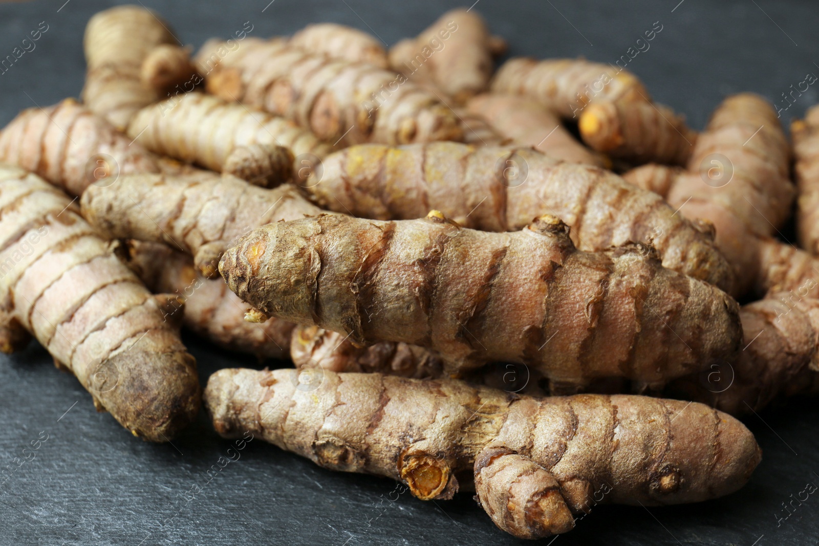 Photo of Many raw turmeric roots on black textured table, closeup