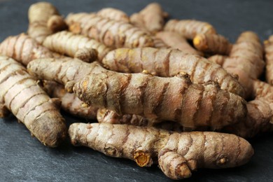 Photo of Many raw turmeric roots on black textured table, closeup