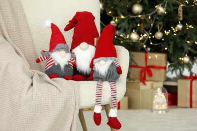 Photo of Funny Christmas gnomes on armchair near decorated tree indoors