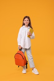 Photo of Happy schoolgirl with backpack and book on orange background