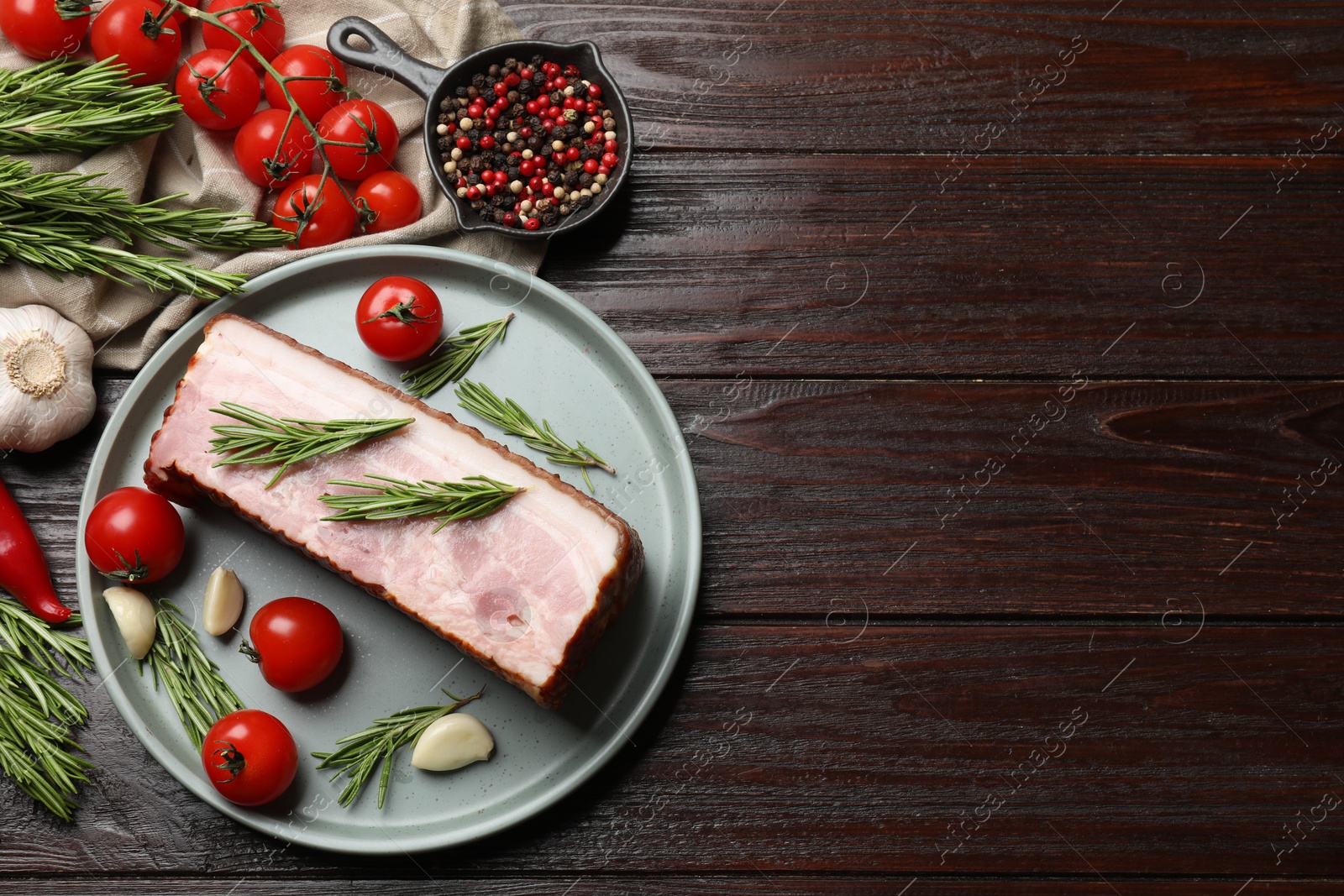 Photo of Piece of raw bacon with spices and cherry tomatoes on wooden table, flat lay. Space for text