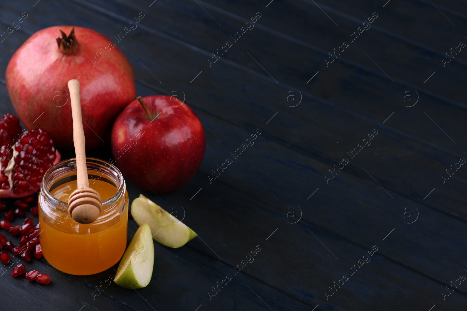 Photo of Honey, apples and pomegranate on dark blue wooden table, space for text. Rosh Hashanah holiday