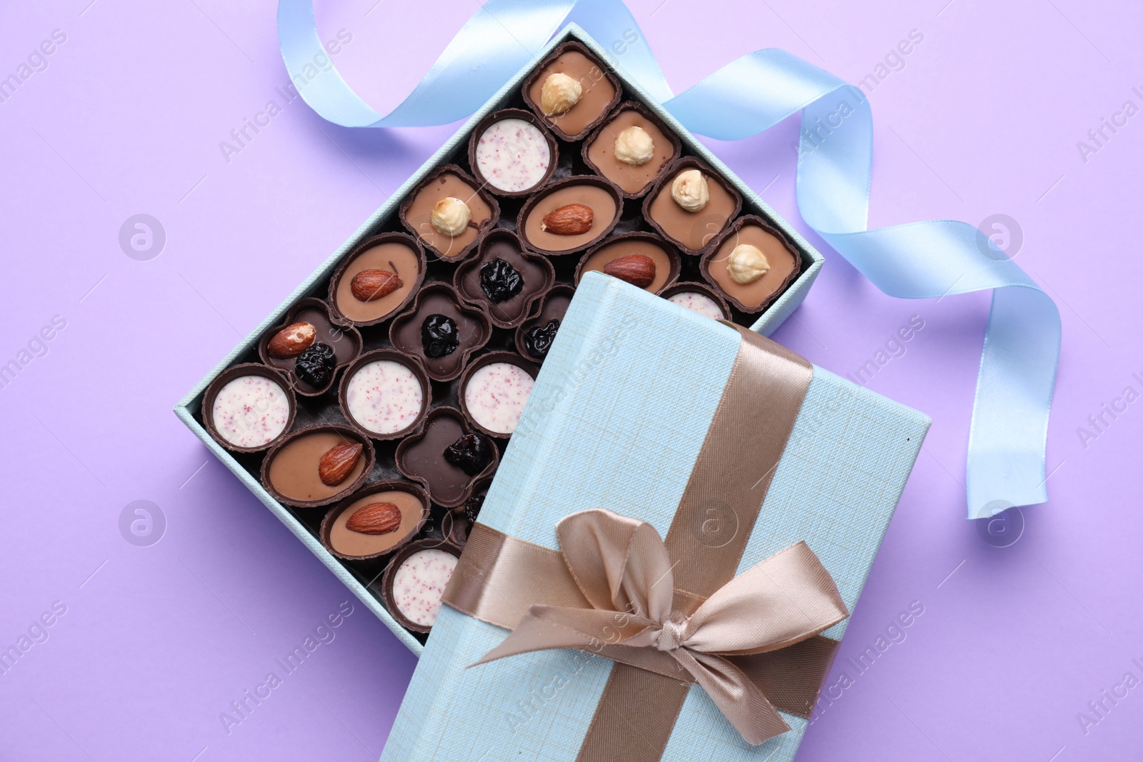 Photo of Open box of delicious chocolate candies on violet background, flat lay