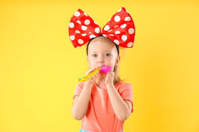 Photo of Little girl with large bow and party horn on yellow background. April fool's day