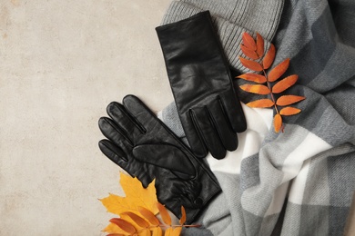 Photo of Stylish black leather gloves, scarf and dry leaves on beige table, flat lay. Space for text
