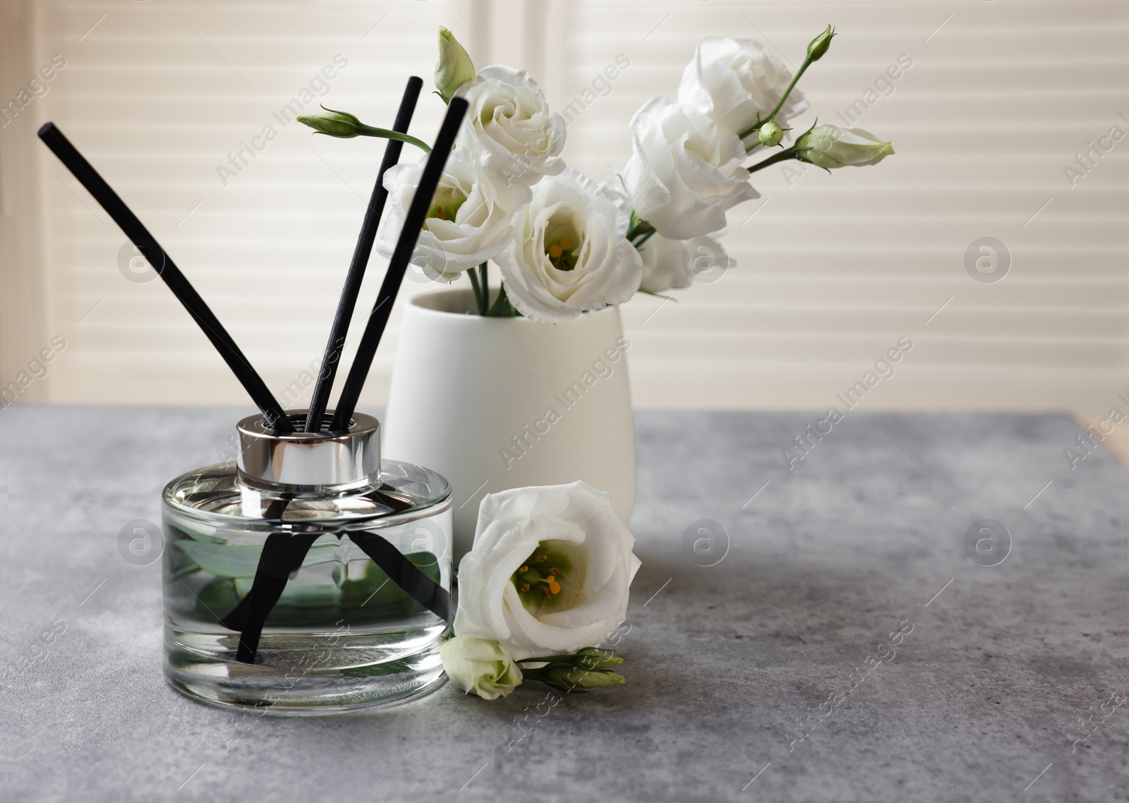 Photo of Reed diffuser and vase with eustoma flowers on gray marble table, space for text