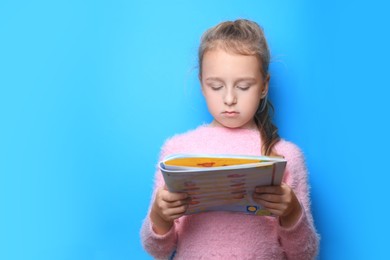 Little girl reading book on light blue background. Space for text