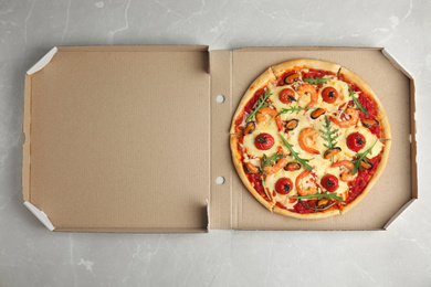 Photo of Delicious seafood pizza in cardboard box on grey marble table, top view