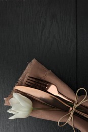 Stylish setting with cutlery, flower and napkin on black wooden table, top view. Space for text