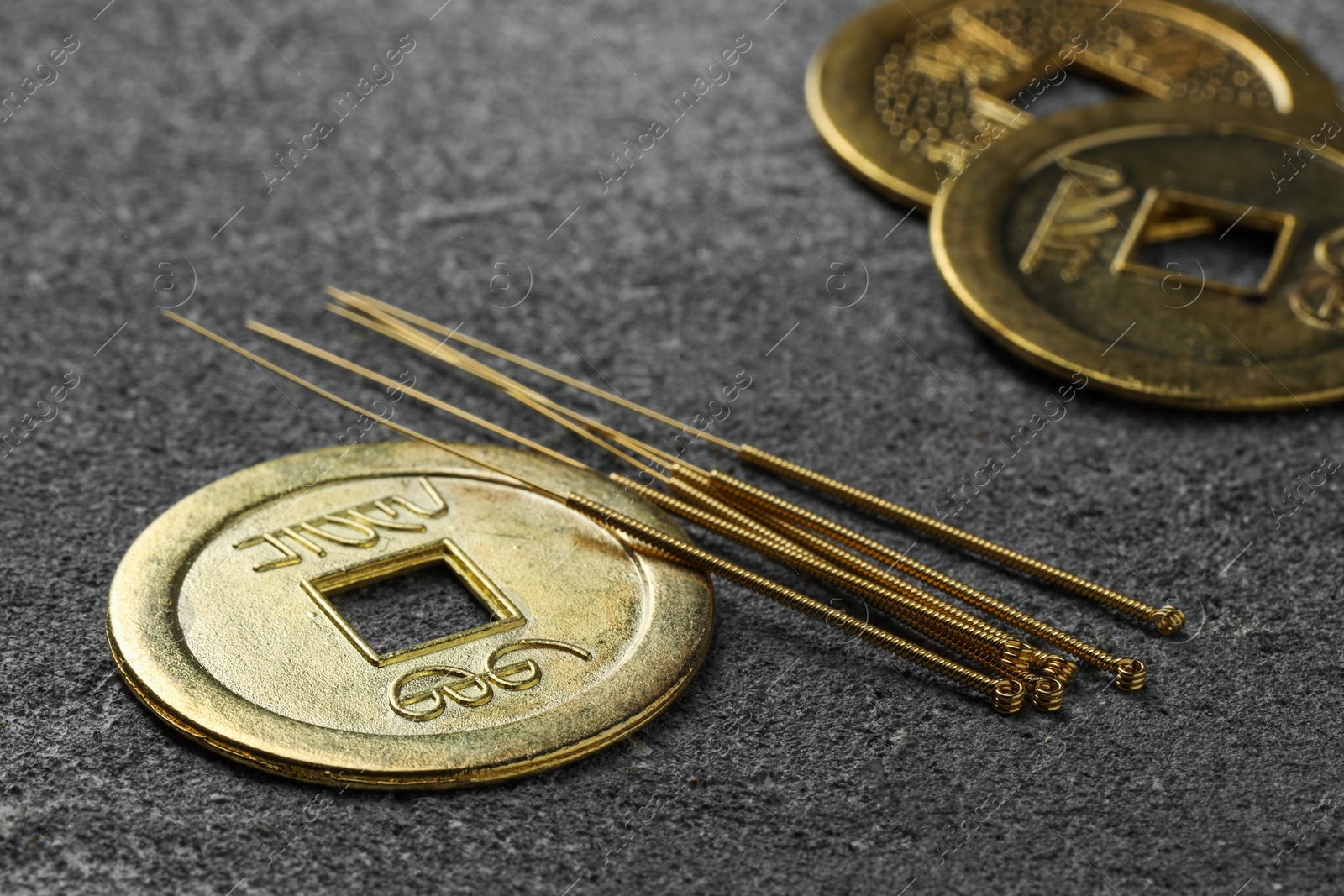 Photo of Acupuncture needles and ancient coins on grey textured table, closeup