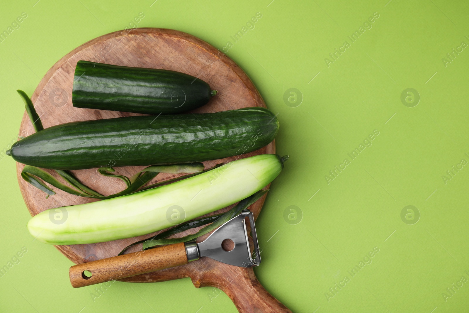 Photo of Fresh cucumbers and peeler on green background, top view. Space for text