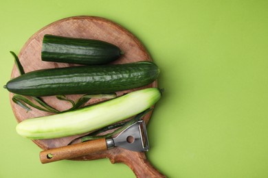 Photo of Fresh cucumbers and peeler on green background, top view. Space for text