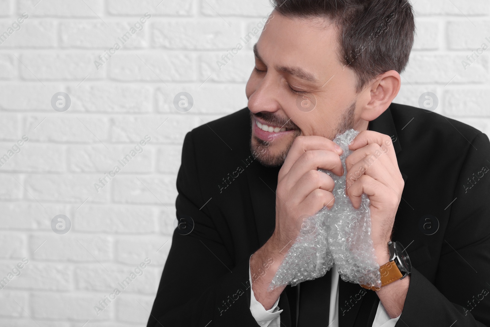 Photo of Stress relief. Businessman popping bubble wrap near brick wall, closeup view. Space for text