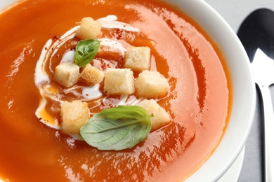 Bowl of sweet potato soup with croutons and basil on table, closeup