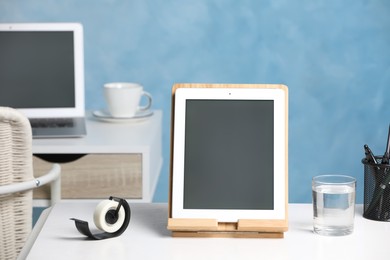 Photo of Modern tablet, glass of water and stationery on white desk