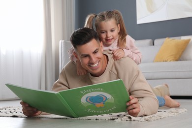 Photo of Father and his daughter reading book at home. Floor heating concept