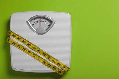 Photo of Weight loss concept. Scales and measuring tape on green background, top view. Space for text