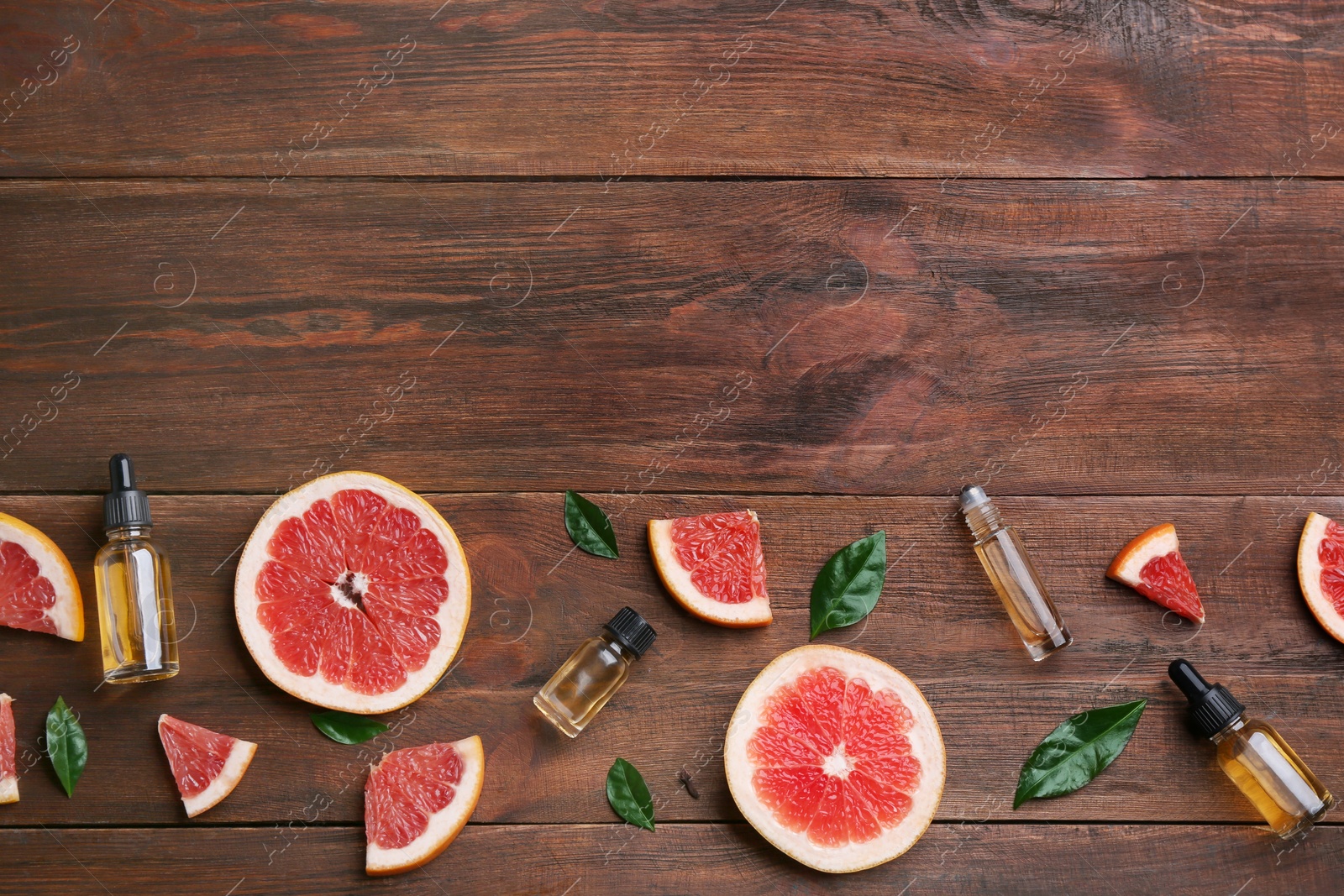 Photo of Flat lay composition with grapefruit slices and bottles of essential oil on wooden background, space for text