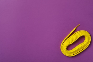 Photo of Yellow shoelace on purple background, top view. Space for text