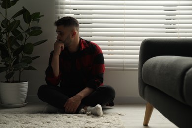 Photo of Sad man sitting near closed blinds indoors