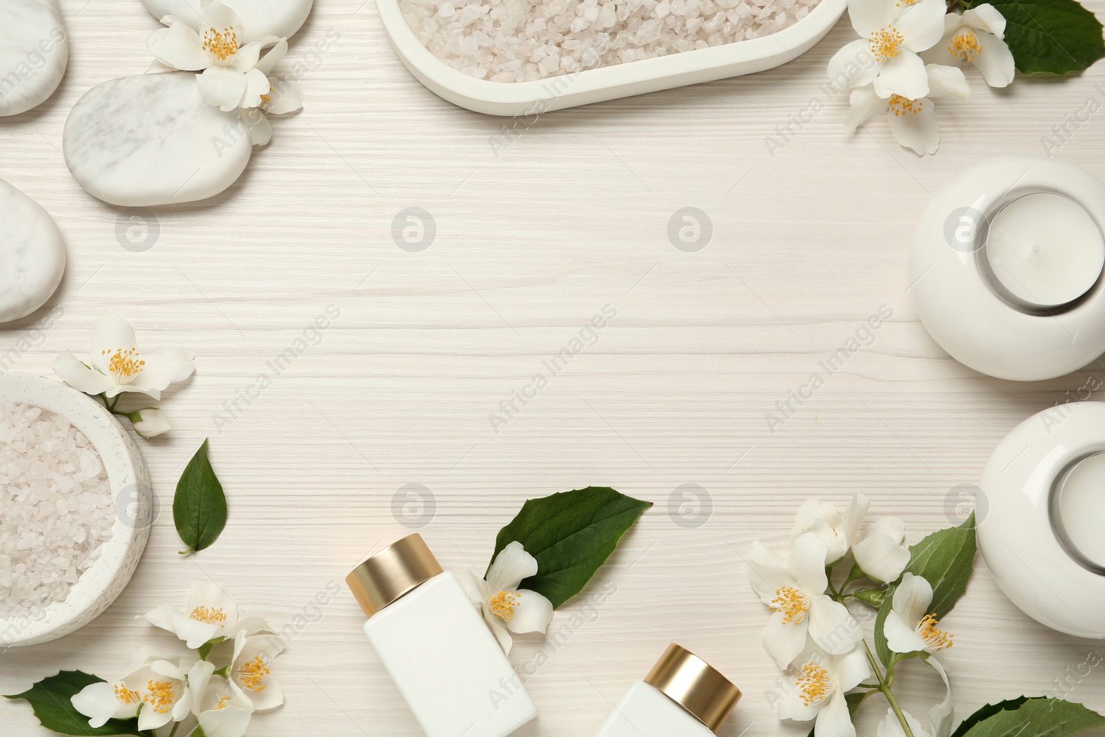 Photo of Frame of beautiful jasmine flowers, spa stones and skin care products on white wooden table, flat lay. Space for text