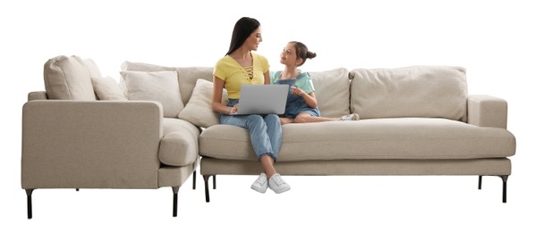 Young woman and her daughter with laptop on comfortable sofa against white background