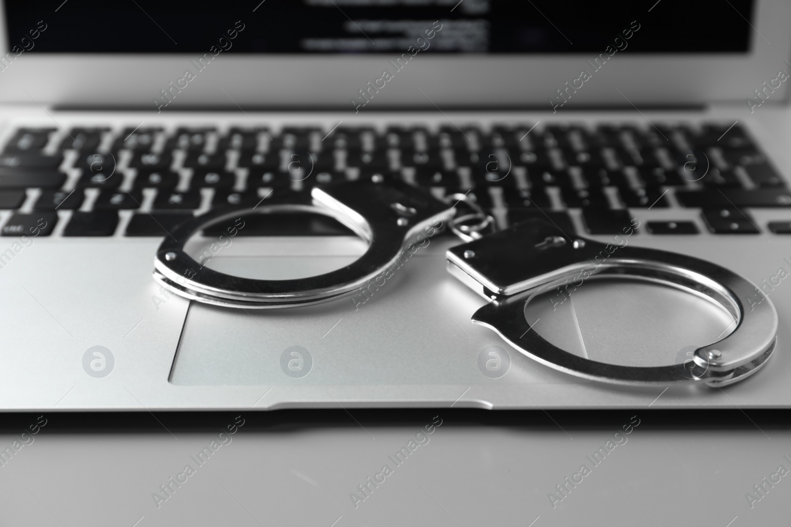 Photo of Modern laptop and handcuffs on table, closeup. Cyber crime