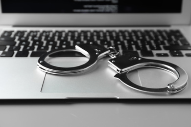 Photo of Modern laptop and handcuffs on table, closeup. Cyber crime