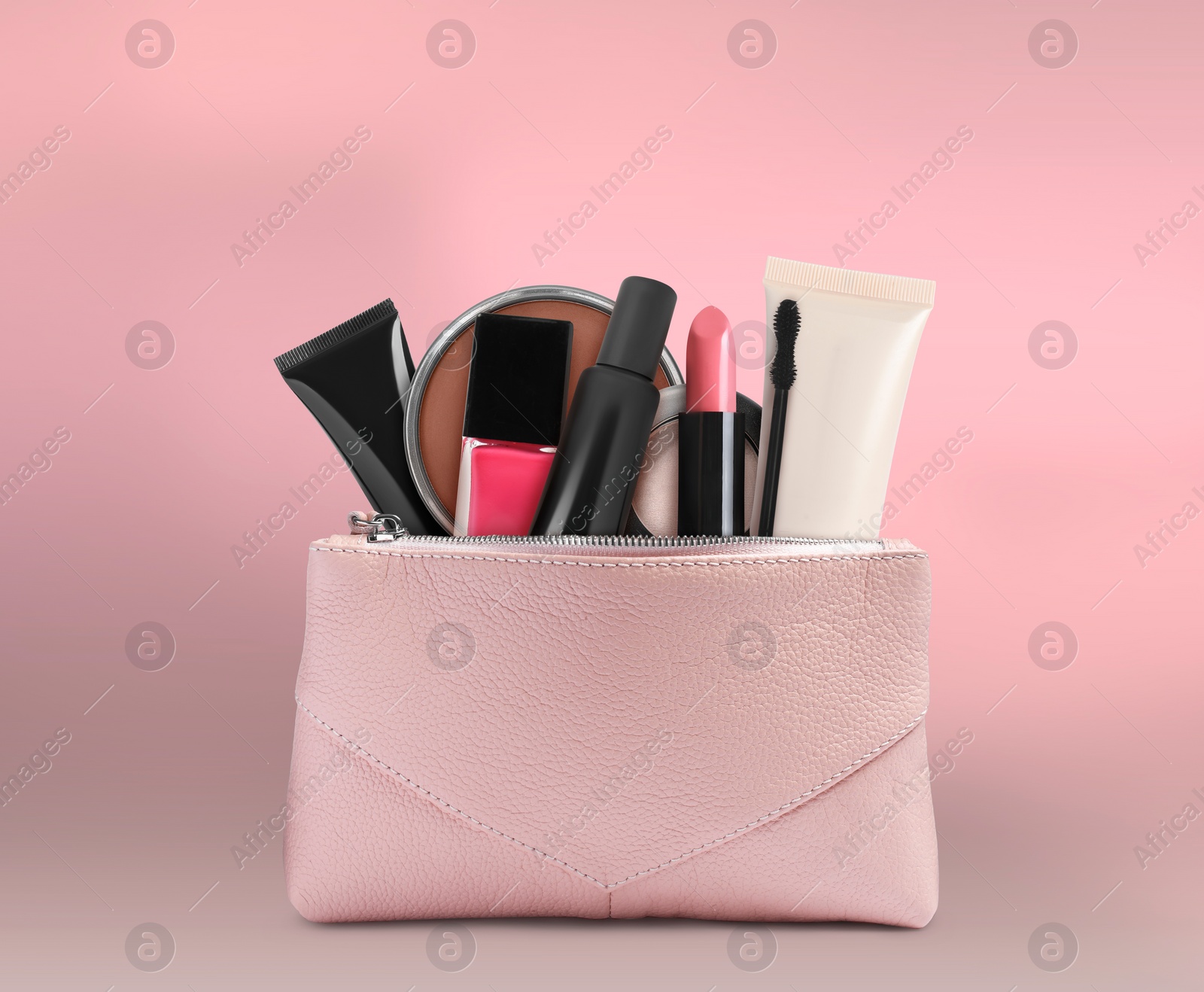 Image of Cosmetic bag filled with makeup products on pink background