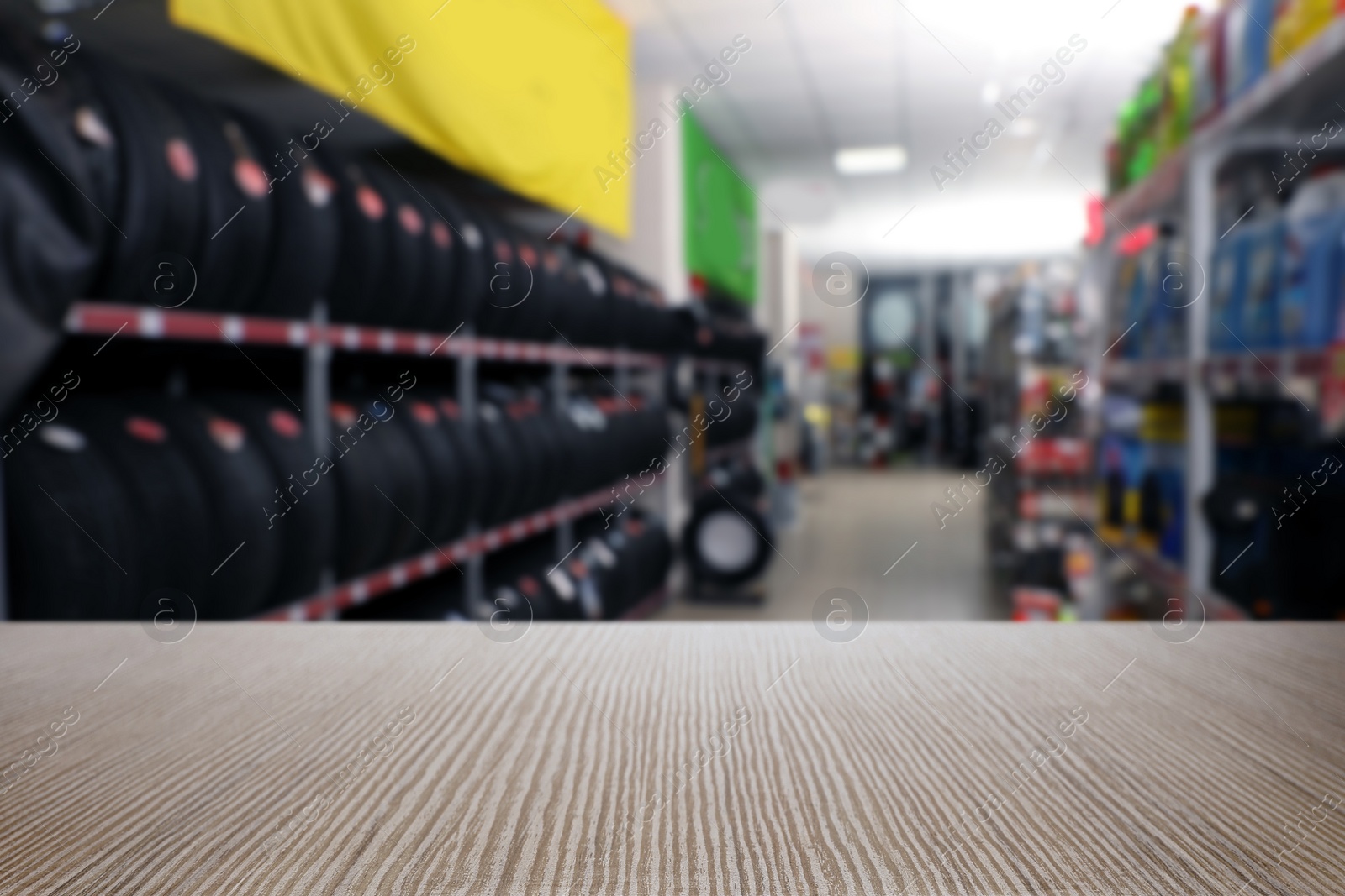 Image of Empty wooden surface and blurred view of car tires in auto store, closeup. Space for text 