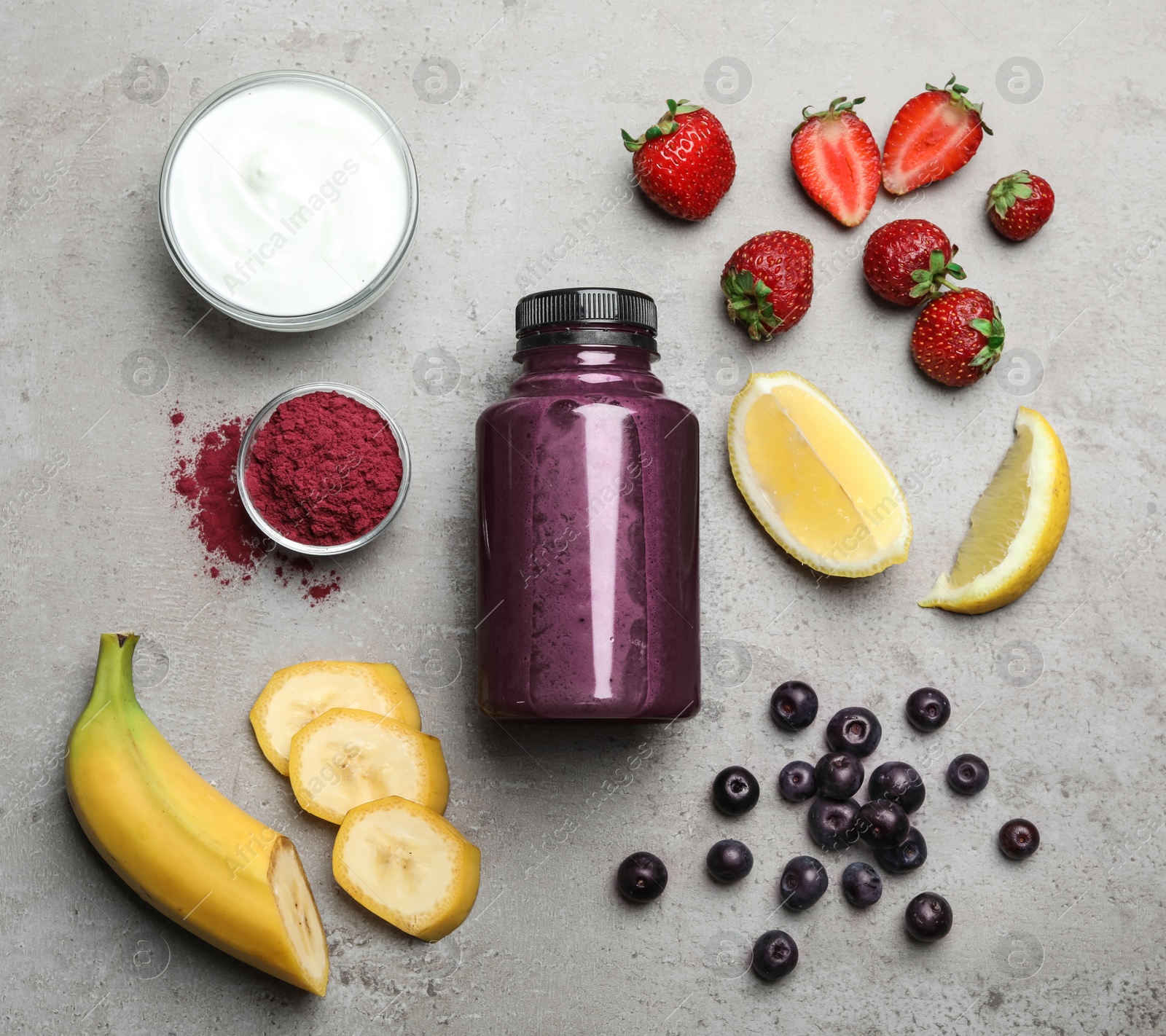 Photo of Bottle of acai drink and ingredients on grey background, flat lay