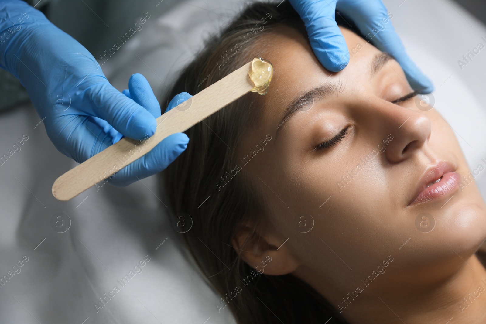 Photo of Young woman undergoing hair removal procedure on face with sugaring paste in salon