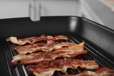 Photo of Slices of tasty fried bacon in grill pan indoors