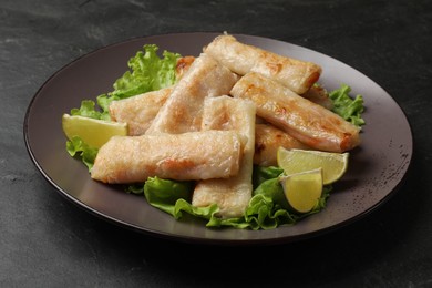 Photo of Plate with tasty fried spring rolls, lettuce and lime on dark textured table, closeup