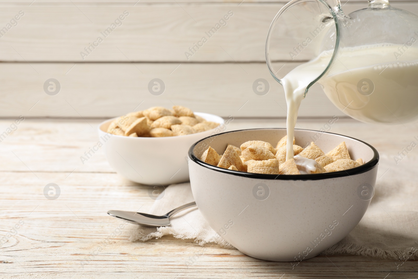 Photo of Pouring milk into bowl of tasty corn pads served on white wooden table. Space for text