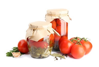 Pickled tomatoes in glass jars and products on white background