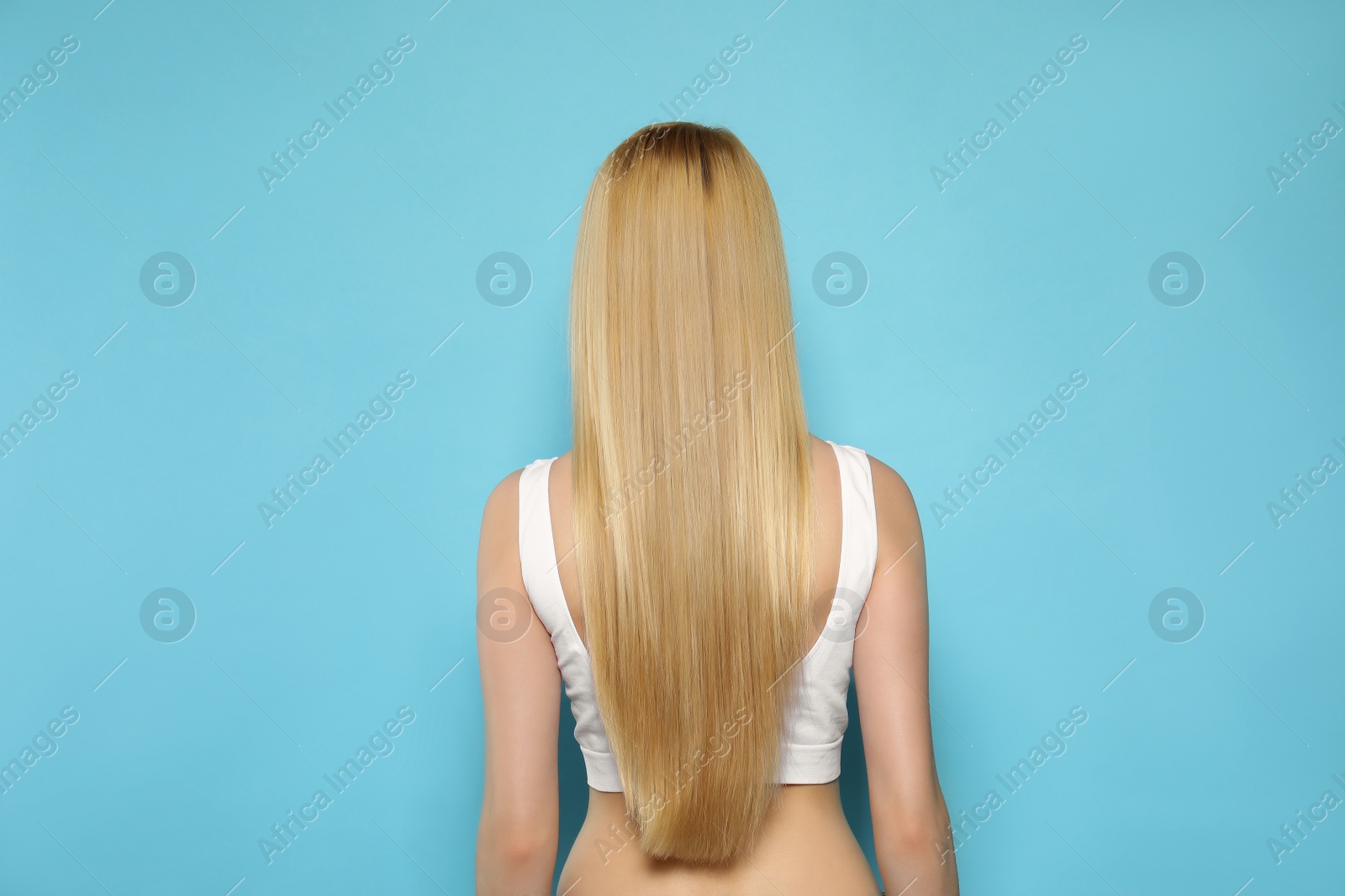 Photo of Young woman with long straight hair on light blue background, back view